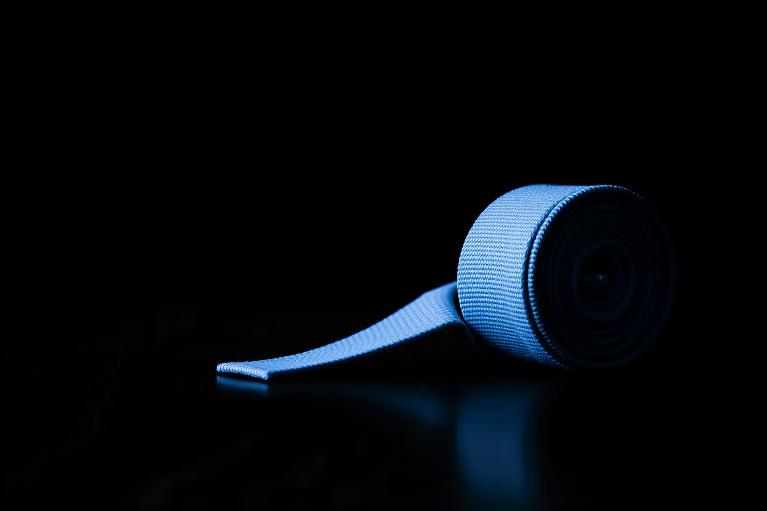 Une ceinture bleue de karaté enroulée sur fond sombre.